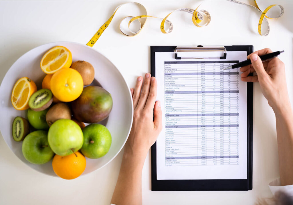 Uma nutricionista e definir um plano alimentar. Ao lado um prato de frutas e em cima uma fita métrica.